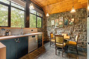 A kitchen with a stone wall, wooden ceiling, and a dining area with chairs and a table.