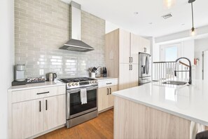Eine moderne Küche mit Edelstahlherd, -backofen und -kühlschrank, hellen Holzschränken und einer weißen Fliesenrückwand.
