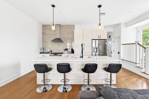 A modern kitchen with a central island, bar stools, and a staircase leading to a balcony.