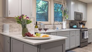 Cozinha moderna com bancada de mármore, eletrodomésticos de aço inoxidável e vista para o exterior.