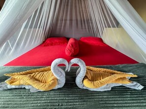 A bed with a red mattress, white net canopy, and two swan-shaped pillows.