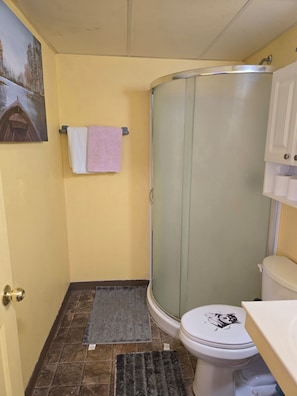 Un baño con cabina de ducha, inodoro, lavamanos y un perchero con toallas.