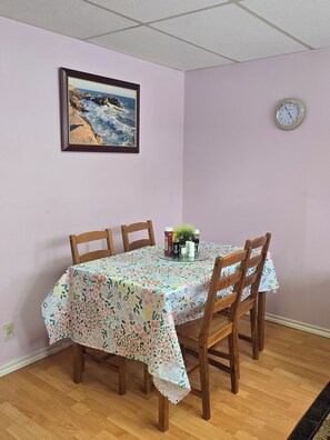 Un comedor con una mesa dispuesta para cuatro, un reloj en la pared y un cuadro enmarcado sobre la mesa.