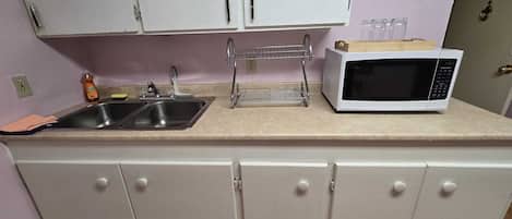 Una kitchenette con un lavamanos, un microondas y un escurreplatos.