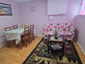 Un área de comedor con una mesa y sillas, un sofá floral, un reloj en la pared y un enchufe.
