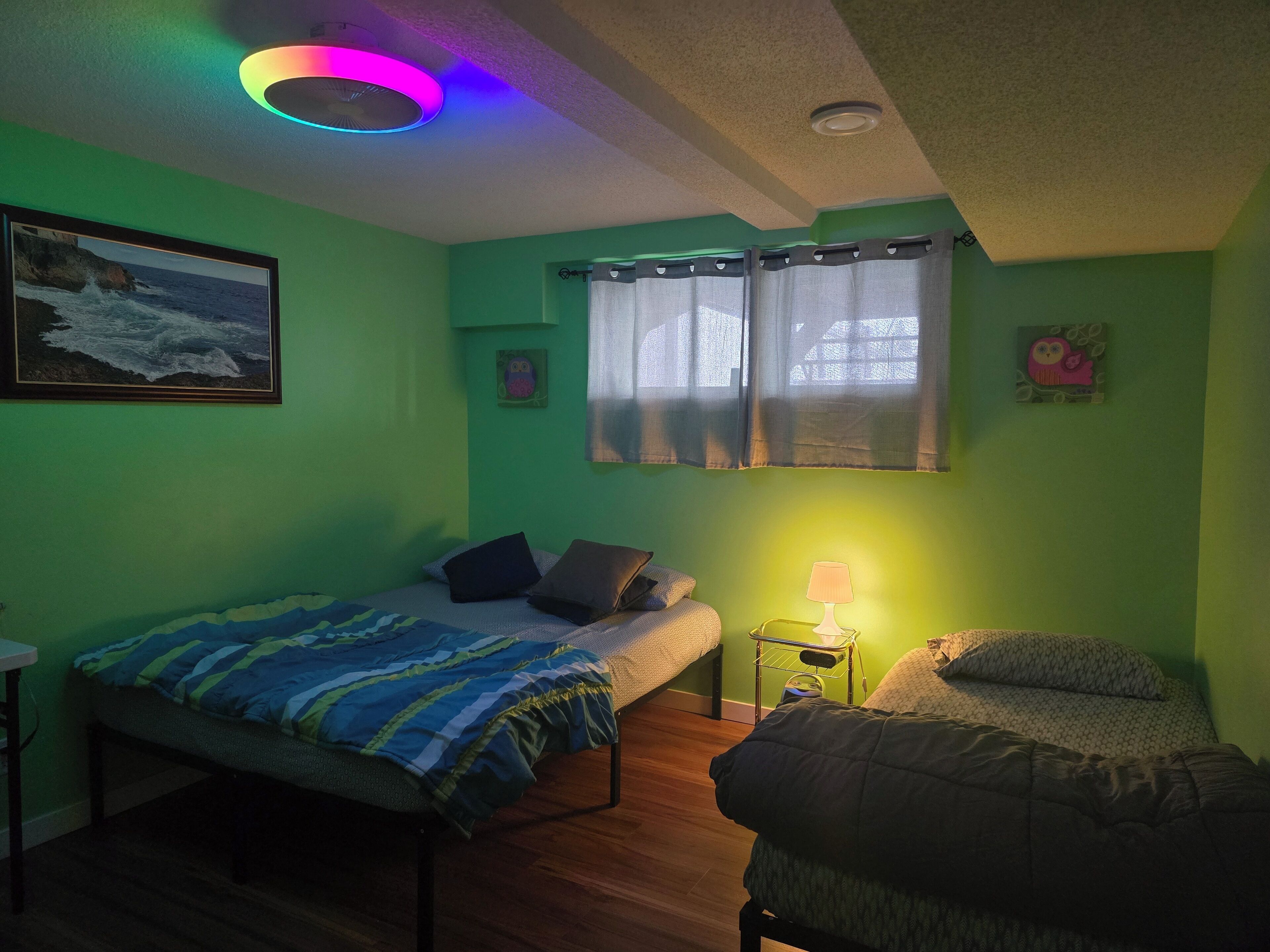 A room with a bed, a chair, a small table, a lamp, and a painting on the wall.