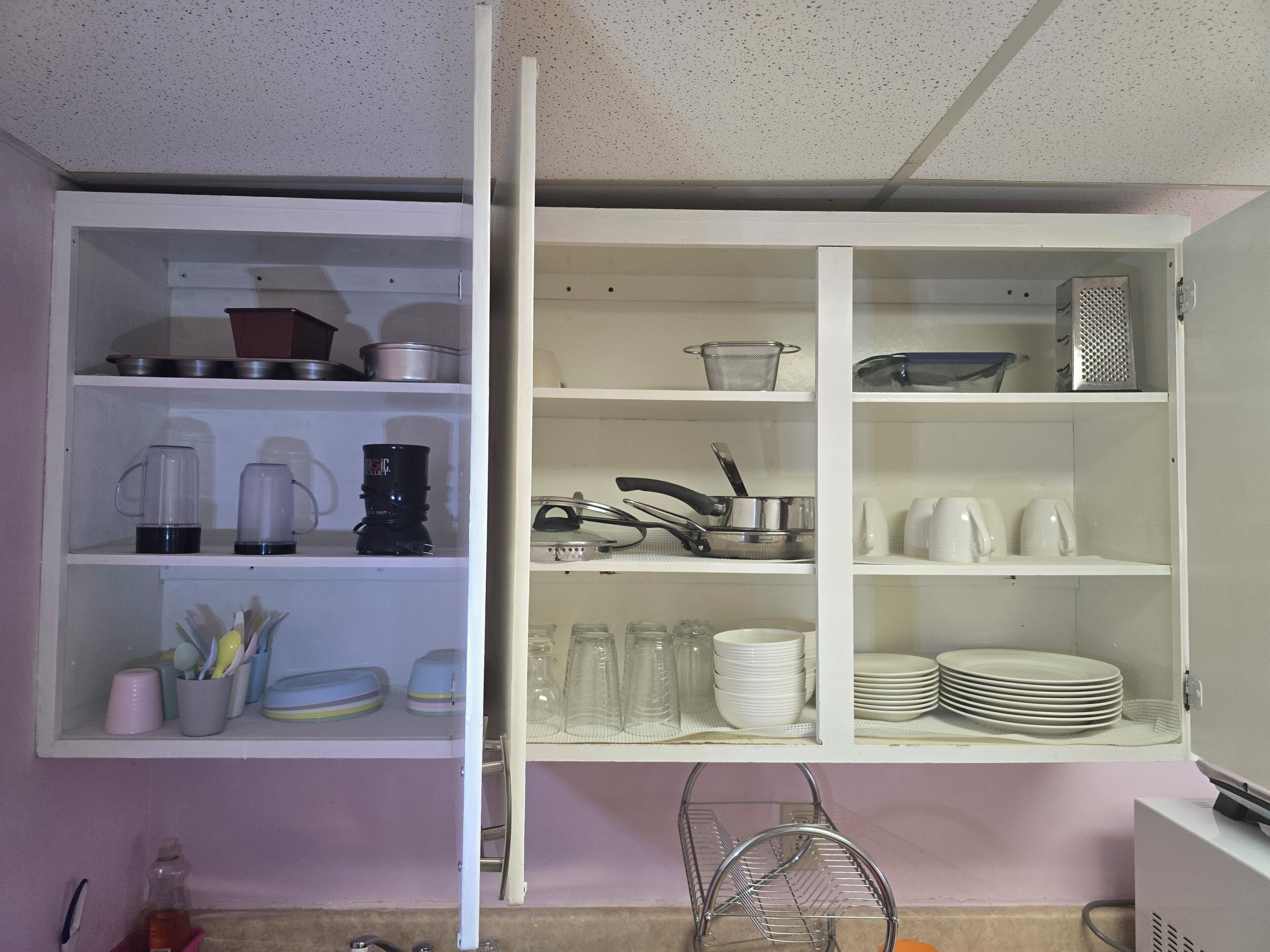 An open kitchen cabinet with shelves containing kitchenware, a coffee maker, and a kettle.