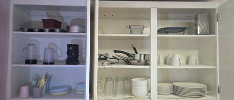 An open kitchen cabinet with shelves containing kitchenware, a coffee maker, and a kettle.