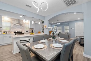 Eine moderne Küche mit Kochinsel, Essbereich mit Marmortisch und Wohnbereich mit Sofa und Zimmerpflanzen.