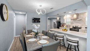 Una cocina moderna con una isla central, un comedor con mesa de mármol y una sala de estar con televisor de pantalla plana.