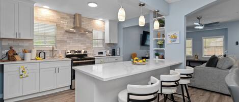 Una cocina moderna con gabinetes blancos, una isla central con taburetes y un horno empotrado, además de un ventilador de techo.