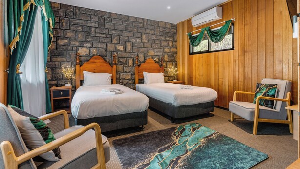 Une chambre d’hôtel avec deux lits, un mur en pierre, un lambris en bois, une fenêtre avec des rideaux, une chaise et un tapis.