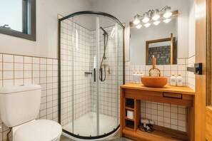 A bathroom with a glass-enclosed shower, a white toilet, a wooden vanity with a sink, and a mirror above the vanity. - Little Acorn - Sun-Kissed Forest Garden, Emerald (Emerald)