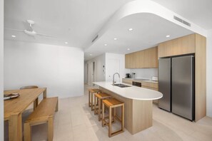 Eine moderne Küche mit einer zentralen Kochinsel, Holzbarhocker, einem Edelstahlkühlschrank und Einbaulicht.