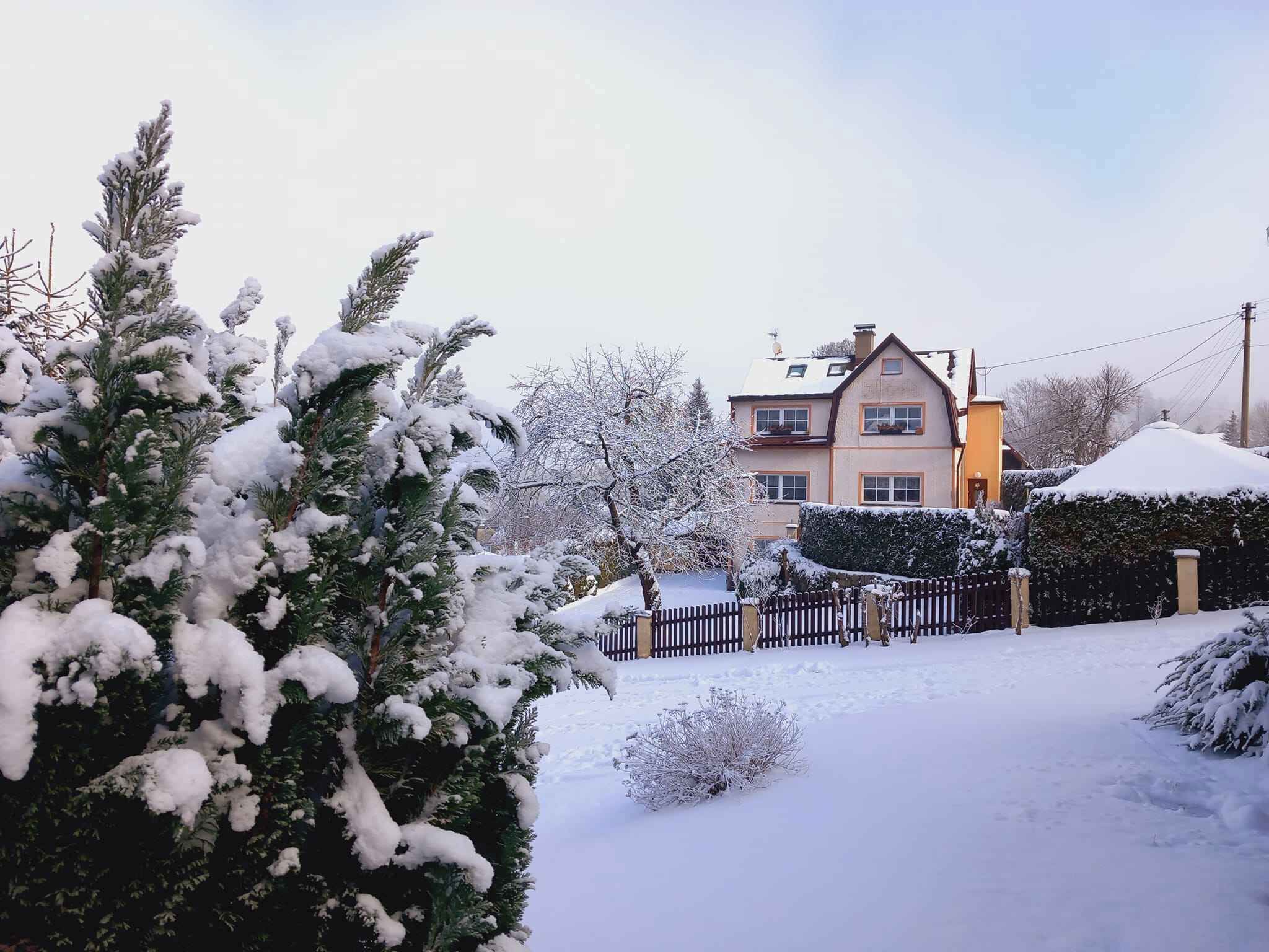 A two-story house with a snow-covered yard and a black fence.