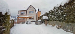 Ein zweistöckiges Haus mit schneebedecktem Dach, einem Holzzaun und einer Steinmauer an einer Seite.