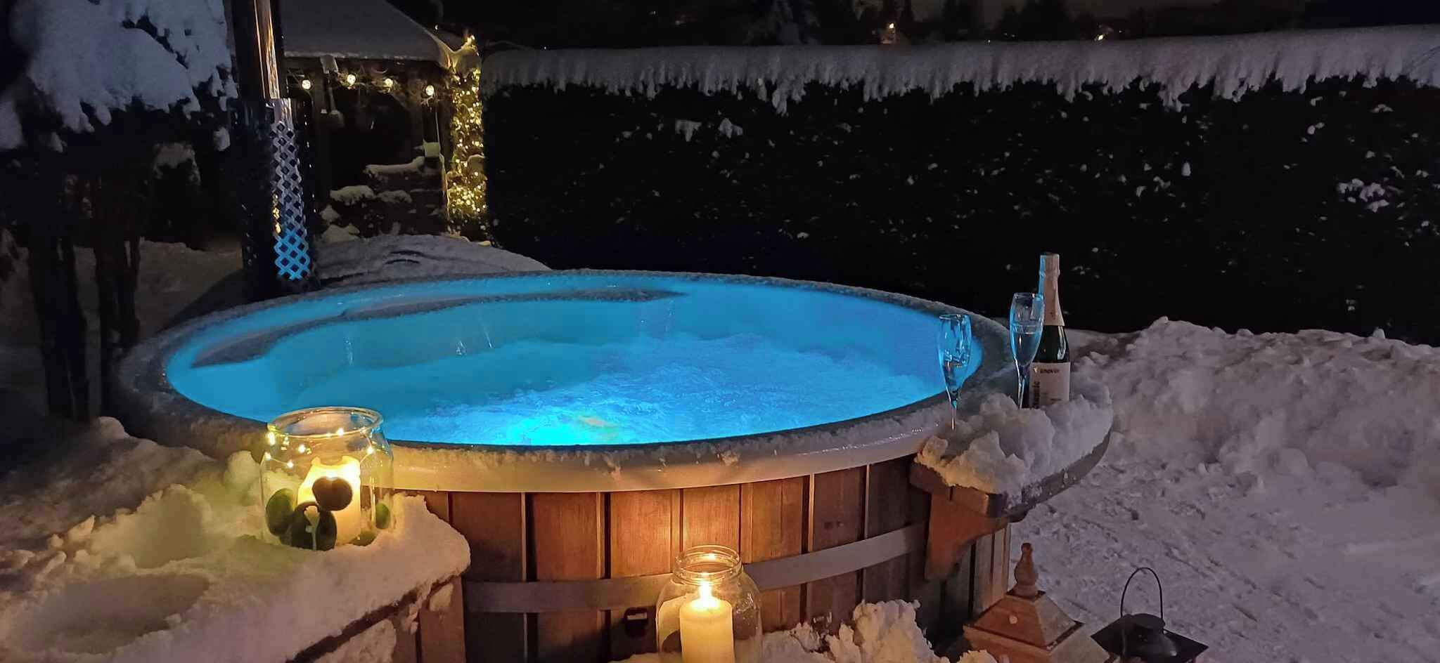 A hot tub surrounded by snow, with candles and a bottle on the edge.