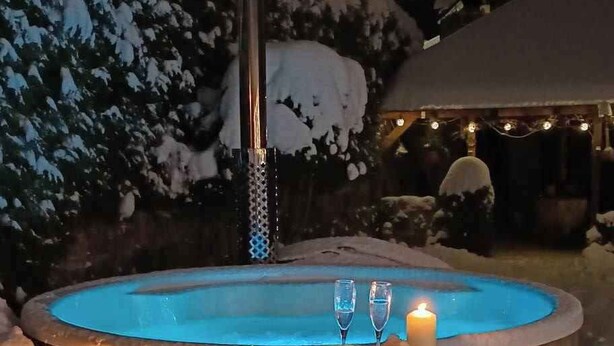 Un jacuzzi de madera rodeado de nieve, con dos velas y faroles encendidos.