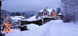 Ein mit Schnee bedecktes Wohngebiet mit Häusern, einem verschneiten Baum und einem klaren Himmel.