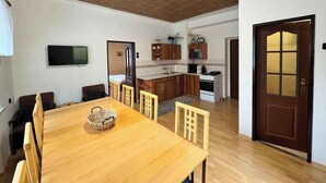 Un comedor con mesa y sillas de madera, una cocina con armarios de madera, un televisor montado en la pared y una puerta de madera con paneles de vidrio.