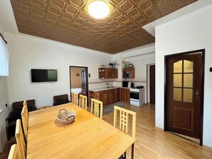 Ein Essbereich mit Holztisch und -stühlen, eine Küche mit Holzschränken, ein an der Wand befestigter Fernseher und eine Holztür mit Fensterfeldern.