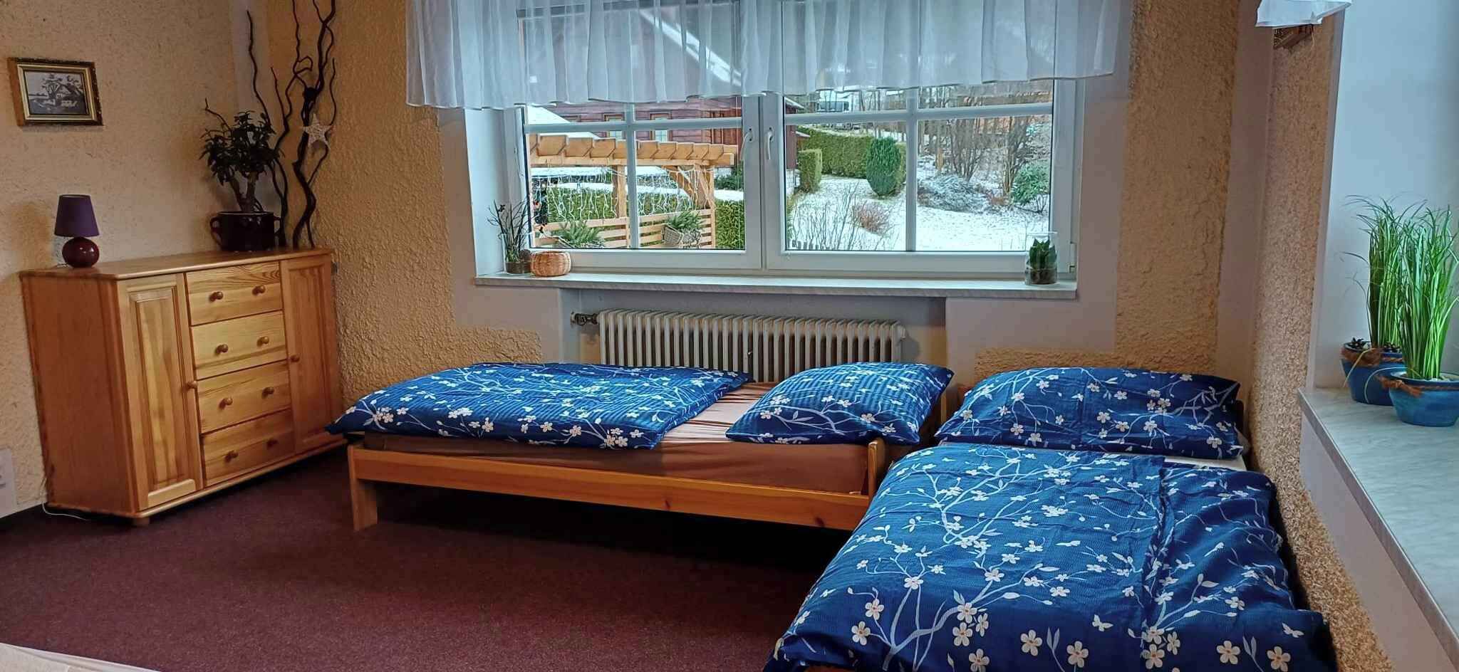A bedroom with two beds, a wooden dresser, a radiator, and a window with a view of a garden.