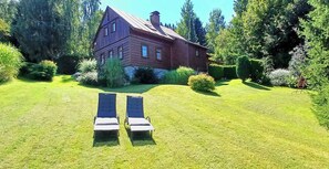 Ein zweigeschossiges Holzhaus mit geneigtem Dach, umgeben von einem gepflegten Rasen und verschiedenen Sträuchern.