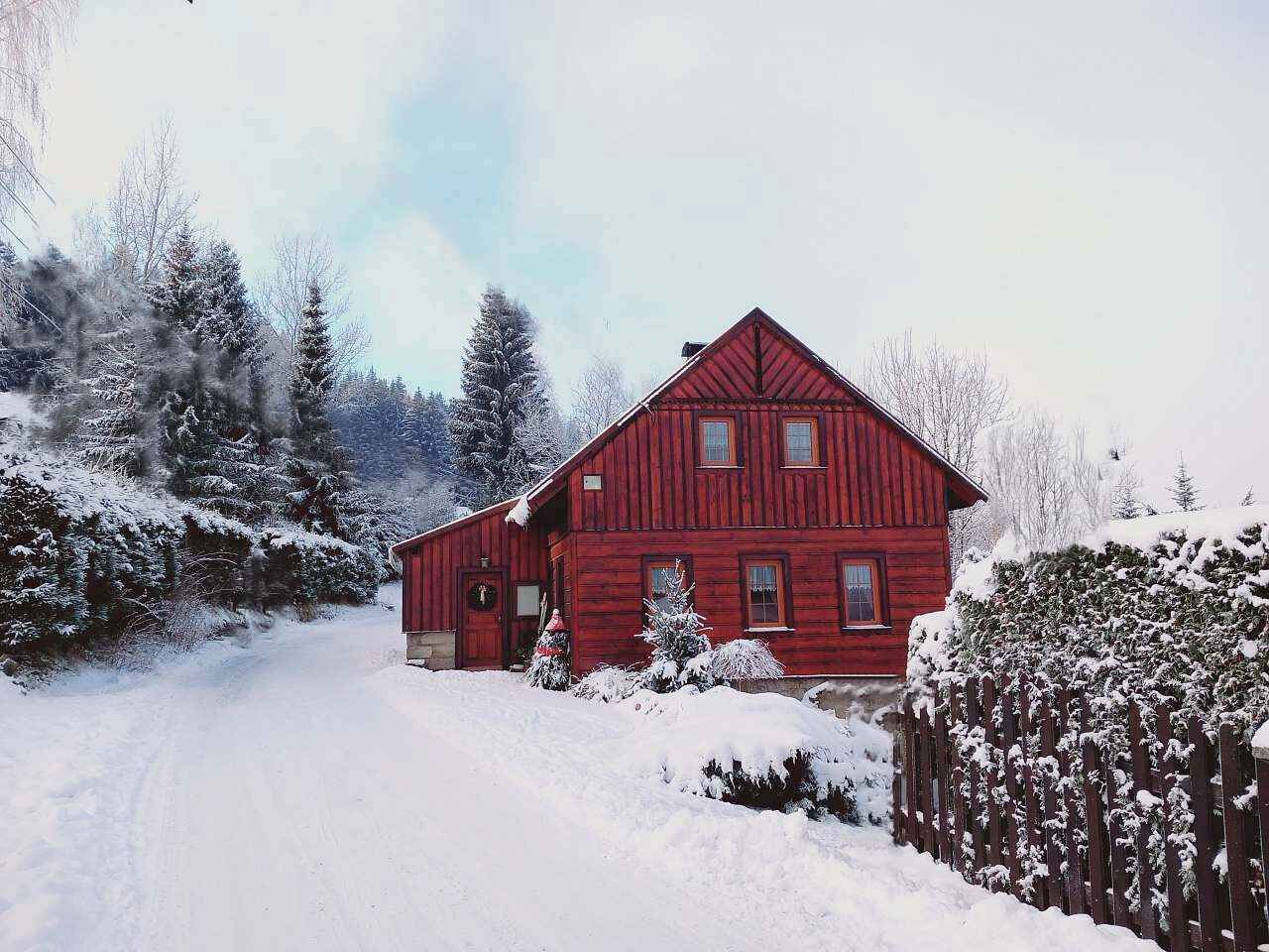 Une maison en bois rouge, avec une allée enneigée et des arbres tout autour.