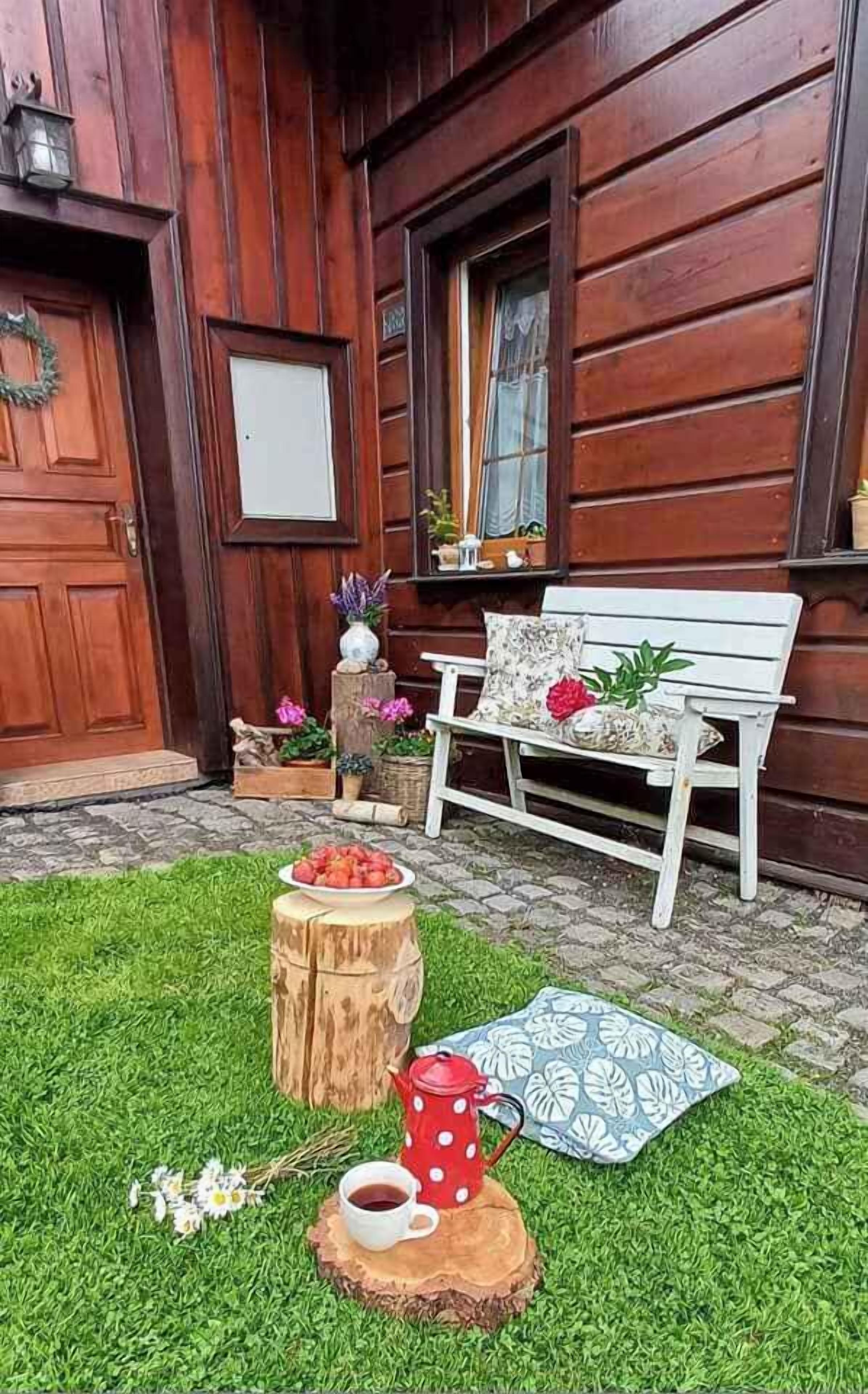 Une cabane en bois avec un banc, une table sur laquelle se trouve une théière et une assiette de fraises.