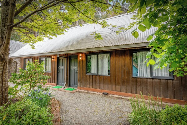 A wooden building with a corrugated metal roof, a front door, and windows with curtains.