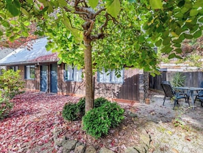 A house with a wooden exterior, a stone foundation, and a covered patio area with outdoor furniture.