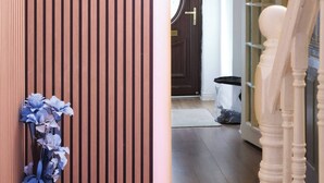 A wooden slat wall, a red vase with flowers, a potted plant, a wooden floor, a door, and a staircase.