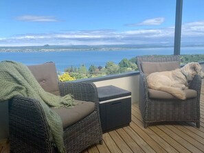 Zwei Korbstühle mit Kissen auf einer Holzterrasse mit Blick auf ein Gewässer.