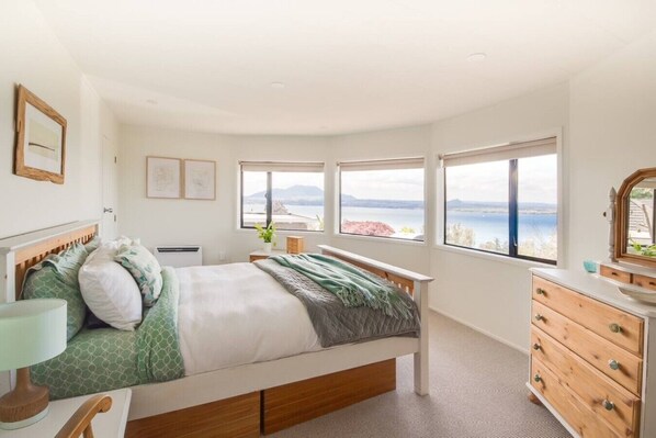 A bedroom with a bed, a dresser, a nightstand, and a window with a view of the water.