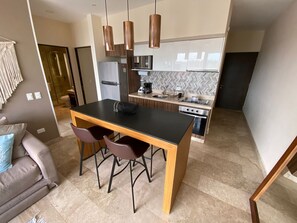 Eine moderne Küche mit einer zentralen Kochinsel, Pendelleuchten und einem Essbereich mit einer Couch und Stühlen.