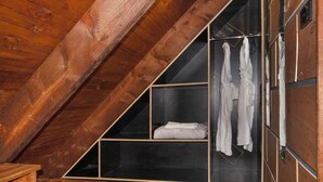 Une chambre mansardée triangulaire avec des poutres en bois, un placard intégré avec une tringle pour suspendre les vêtements et une étagère avec des serviettes pliées.