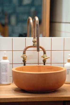 Un lavamanos con grifo de cobre, azulejos blancos y dos botellas de jabón de baño sobre la encimera.