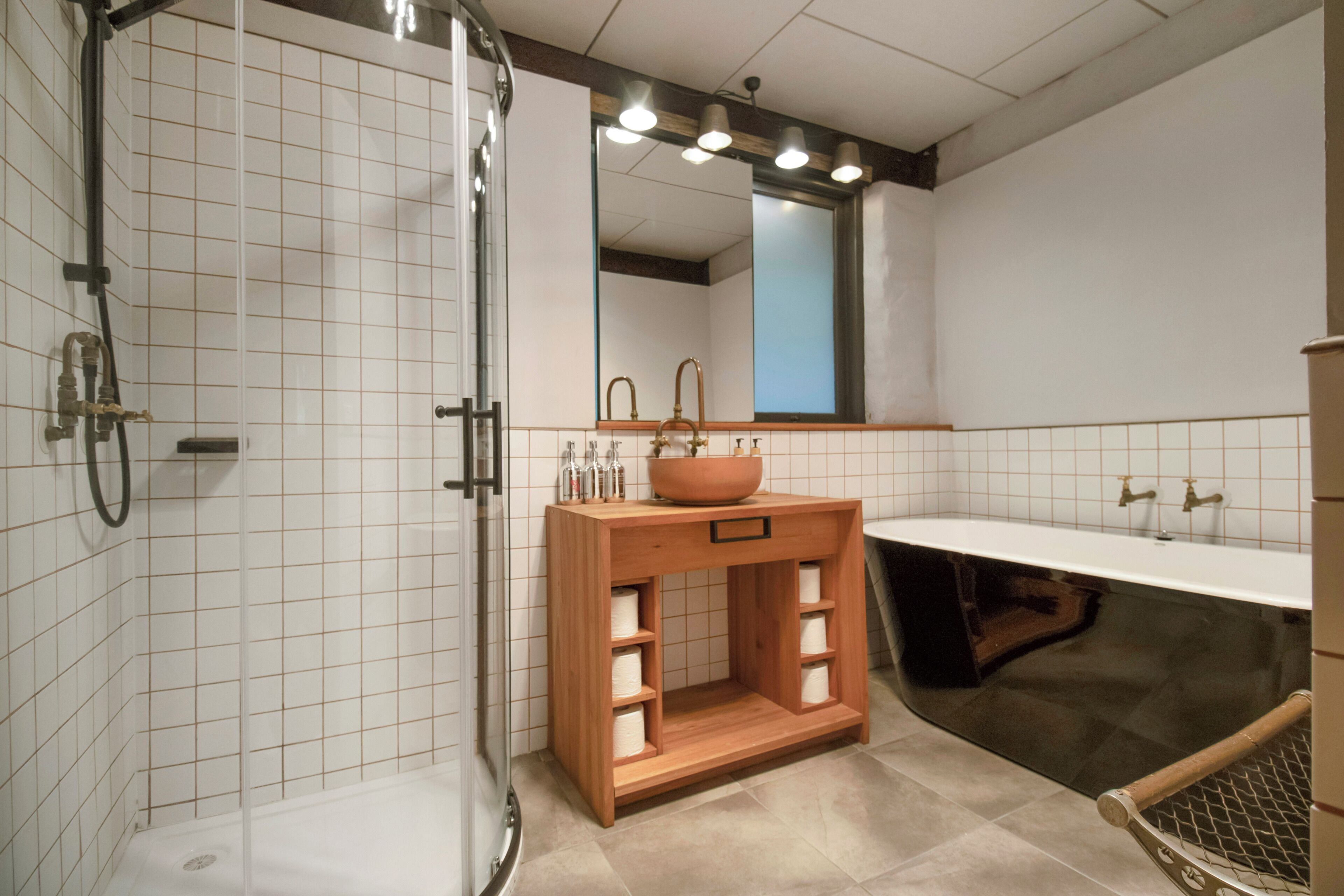 A bathroom with a shower, a sink with a mirror, and a wooden cabinet with shelves.