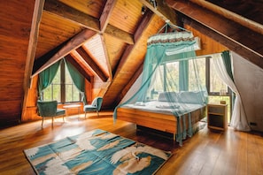 A bedroom with a wooden ceiling, a bed with a canopy, a chair, a small table, and a window with curtains.