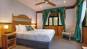 Une chambre d’hôtel avec un grand lit, une tête de lit en bois, une table de chevet, une chaise et une fenêtre avec des rideaux verts.