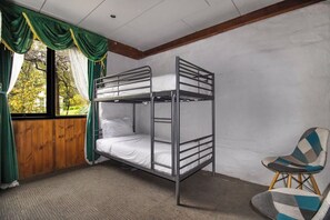 Dormitorio con literas, ventana, cortinas y una silla.