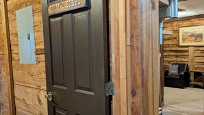 A wooden door with a sign reading 'ROOM & BOARD,' a power outlet, and a wall-mounted light fixture.