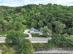 A house surrounded by dense forest, a road, and a small driveway.