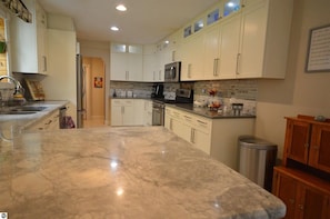 A kitchen with white cabinets, a marble countertop, a stainless steel trash can, and a microwave.