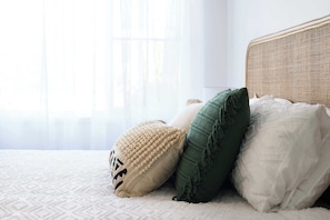 Ein Bett mit weißer Strukturdecke, einem gewobenen Kopfteil und drei Kissen.