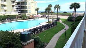 A pool area with a clear view of the ocean, a building with multiple balconies, and a well-maintained lawn. - Coral Reef Retreat | Beachfront Escape (Galveston)