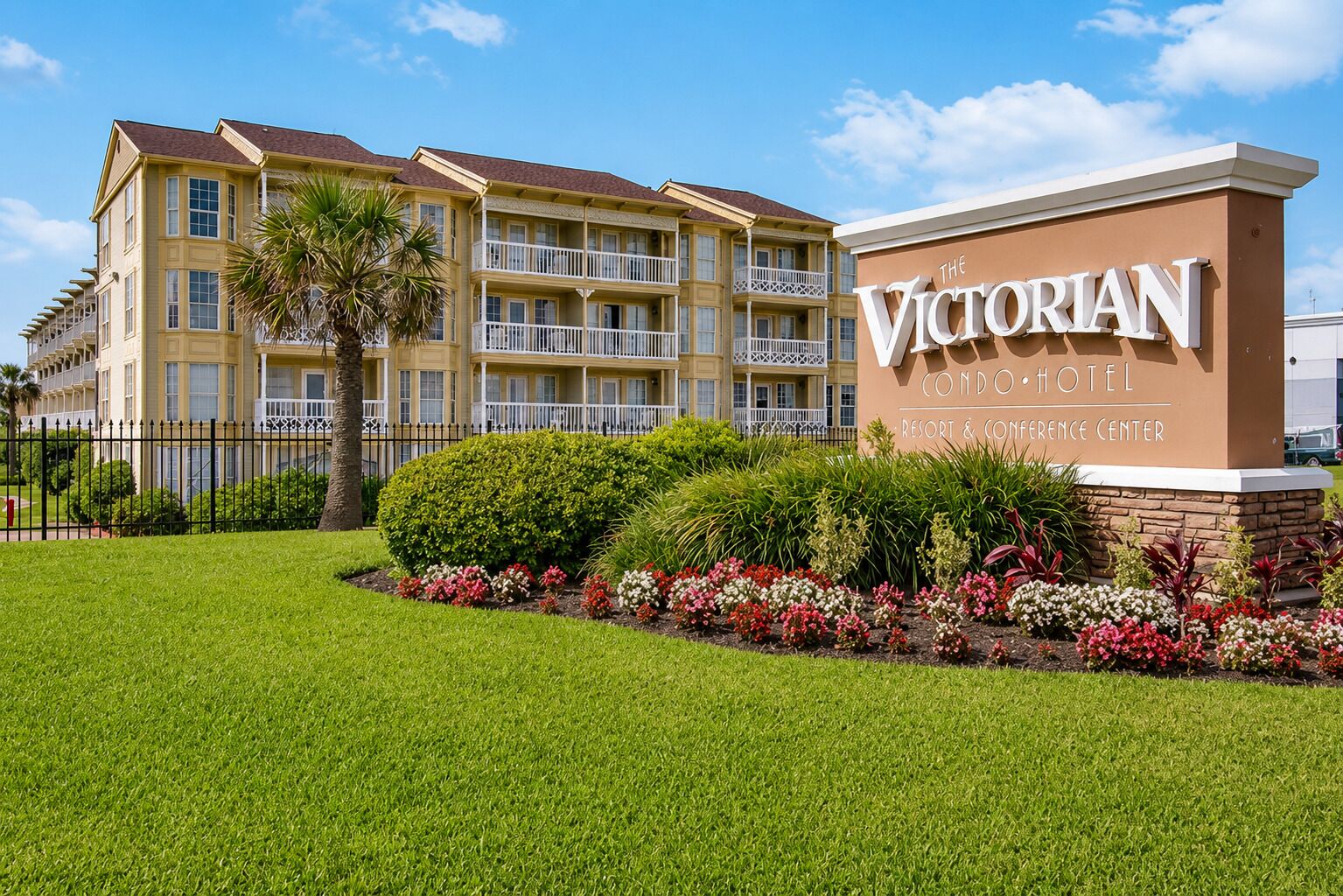 A multi-story building with balconies, a sign for 'The Victorian Condominium Hotel,' and a well-maintained lawn with flower beds.