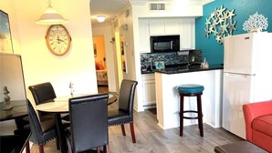 A compact kitchen with white cabinets, a black microwave, and a teal backsplash. - Coral Reef Retreat | Beachfront Escape (Galveston)