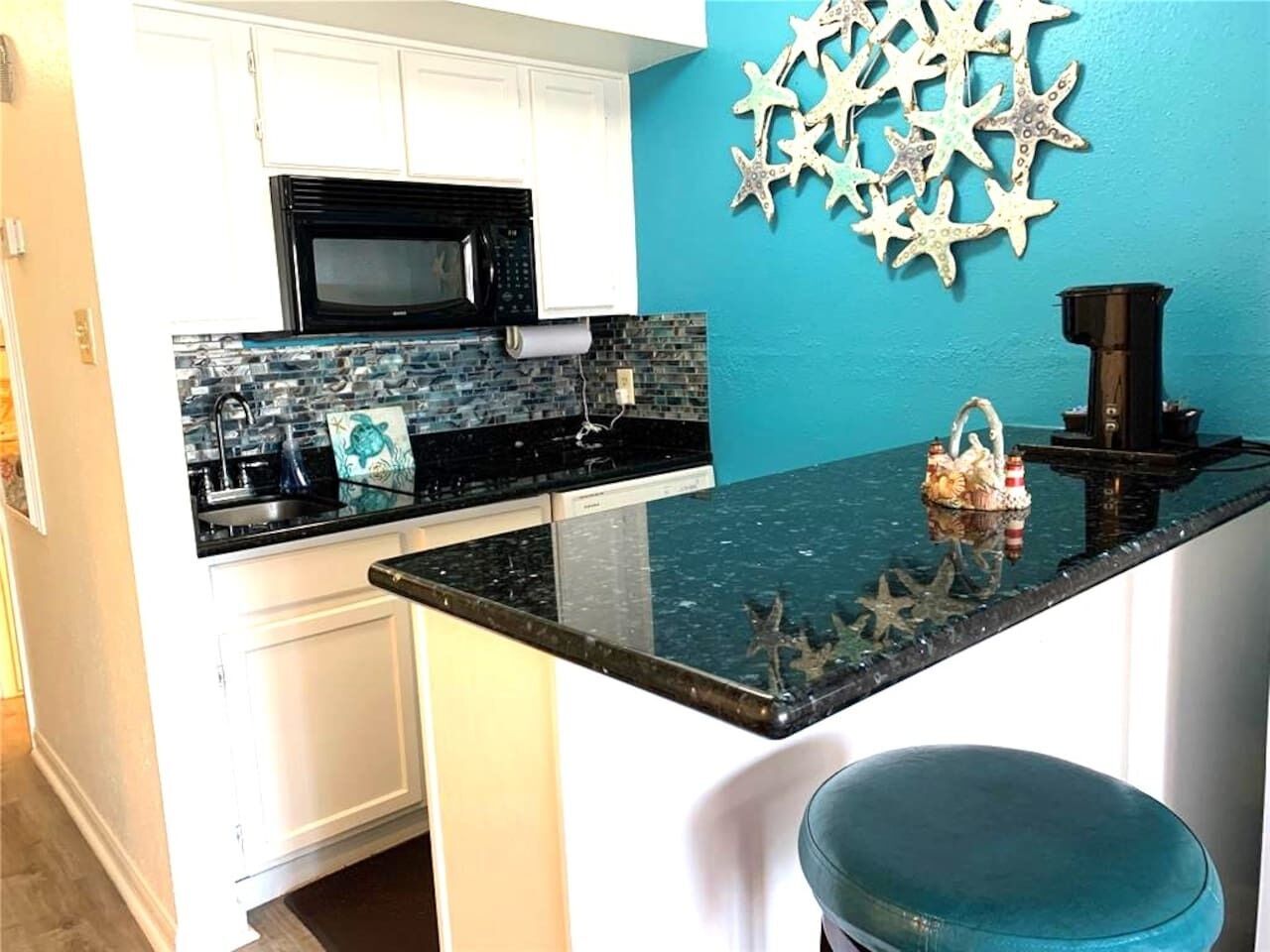 A kitchen with white cabinets, a black microwave, a glass island counter, and a blue wall with starfish decorations.