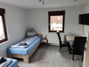 Ein Schlafzimmer mit Bett, Schreibtisch, Stuhl, Heizkörper und Fenster.